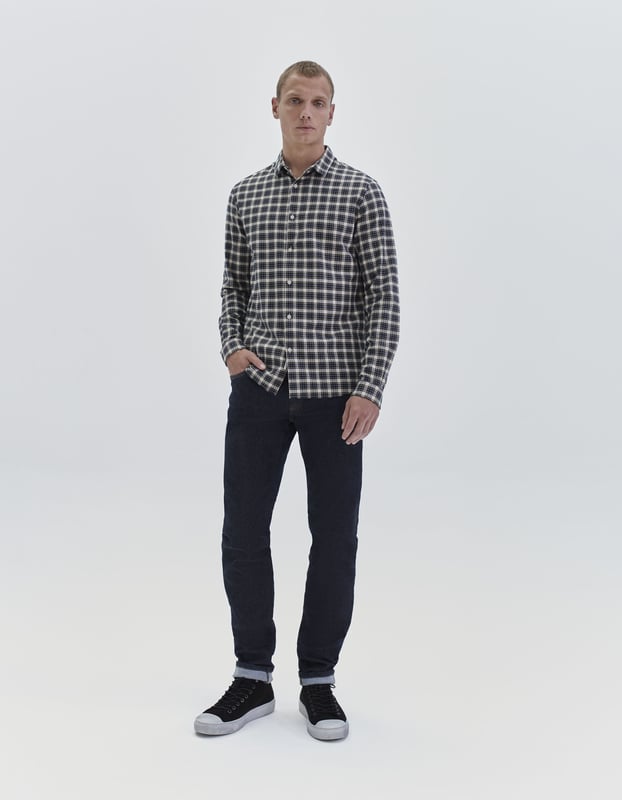 This navy shirt has collared neck and long sleeves. The shape is slim and short, with checked pattern.