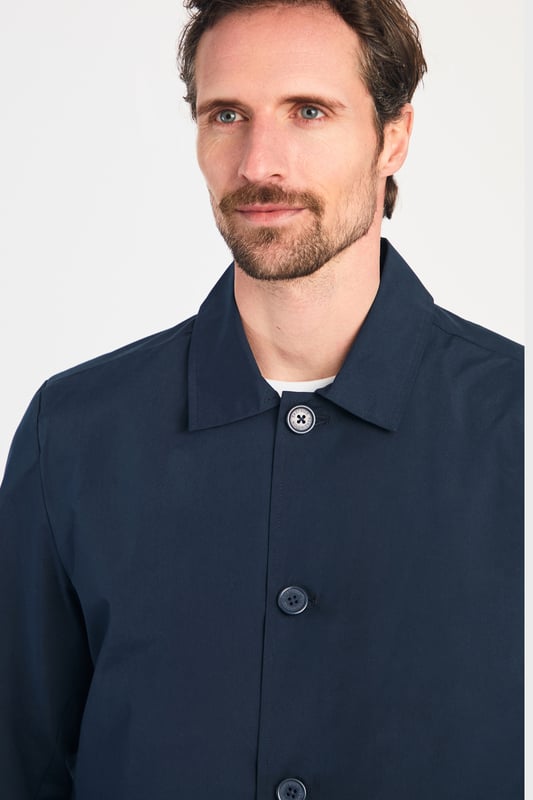 This men's mac-style coat from Kensington Eastside features a classic collar, button-up fastening, and a mid-length cut for a sleek, modern look. Lightweight and stylish, it’s perfect for layering over both casual and formal outfits, making it a versatile wardrobe essential for effortless style.