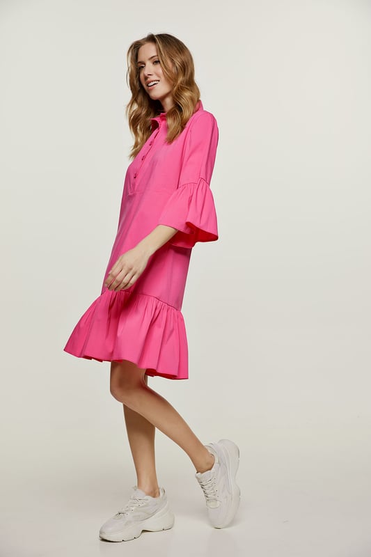 Deze fuchsia jurk is gemaakt van geweven stretch poplin. Het heeft klokkende mouwen van ¾ lengte. De jurk heeft een kraag en een sluiting in de taille met plastic knopen. Een naad onder de buste zorgt voor een perfecte pasvorm. De jurk heeft een brede zoom met ruches. De jurk heeft een losse pasvorm en valt boven de knie.