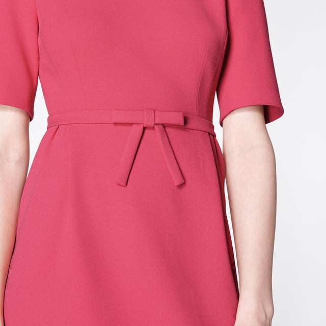 The perfect pink shift, our Elina dress takes its cues from bespoke occasion dresses of an era gone by. Crafted from raspberry pink crepe, it has a round neck, short sleeves, a neat bow belt at the waist and a front panel to the knee-length skirt. Simple and chic, wear it with strappy heels or sleek courts for during the occasion season.