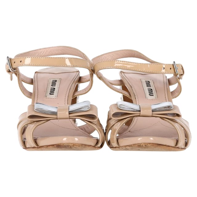 VINTAGE, UVP WIE NEU  
Die Miu Miu Sandalen mit Schleifen-Detail und Knöchelriemen in nude Lackleder sind der Inbegriff glamouröser Eleganz. Aus luxuriösem nude Lackleder gefertigt, verfügen diese Sandalen über ein zartes Schleifen-Detail an der Zehe, das dem Design eine verspielte und gleichzeitig raffinierte Note verleiht. Der Knöchelriemen sorgt für einen sicheren und schmeichelhaften Sitz, während der mit Kristallen besetzte Absatz ein funkelndes, hochmodisches Statement setzt, das jedes Outfit aufwertet. Perfekt für besondere Anlässe oder einen eleganten Abend, bringen diese Miu Miu Sandalen eine einzigartige Kombination aus Feminität, Luxus und glitzerndem Glamour in Ihre Schuhkollektion.   

Miu Miu Sandalen mit Schleifen-Detail und Knöchelriemen in nude Lackleder  

Zustand: Sehr gut  
Gebrauchsspuren: Geringe Abnutzung, leicht gebraucht, aber sehr gut gepflegt. Leichte Markierung an den Sohlen und Faltenbildung, leichte Kratzer an Sohlen und Absätzen.  
Verpackung: Keine  
Farbe: Braun | nude  
Material: Leder | Lackleder  
Größe: EU | 36.5/UK3.5/US6.5  
SKU: NAPPUGBSH444498W