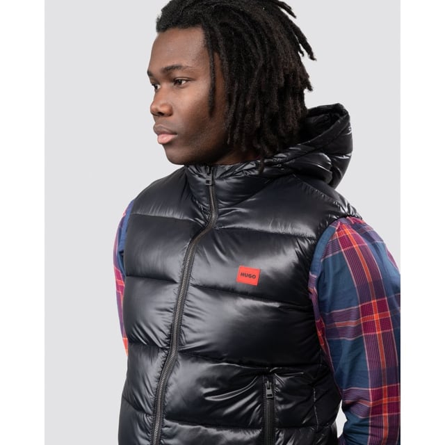 This sporty Water Repellent Puffer Hooded Gilet from HUGO is the perfect piece to elevate your wardrobe this season with sustainable style. Crafted from water-repellent recycled nylon and padded with sustainably sourced recycled fibres providing warmth and comfort. Featuring an insulated hood with full zip closure, elasticated binding and front zip pockets. Finished with a signature HUGO logo patch on the chest.Slim Fit, Water-Repellent Recycled Nylon Shell, Recycled Polyester Padding, Insulated Hood, Full Zip Closure, Twin Zip Front Pockets, Internal Zip Pocket, HUGO Branding. -Style & Fit:Slim Fit, Fits True to Size. Composition & Care:Shell: 100% Recycled Polyamide, Fill: 100% Recycled Polyester, Machine Wash.