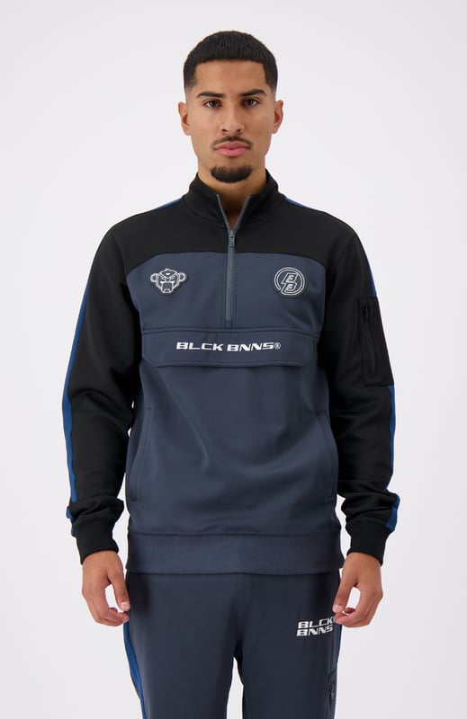 100 % poliéster Cuello alto con media cremallera Camino de convoy en el pecho Bolsillo lateral con cremallera en el brazo izquierdo Solapa distintiva de BNNS en color negro Dos bolsillos delanteros con cremallera Mangas a rayas Se puede combinar con RUMBLE TRACKPANTS