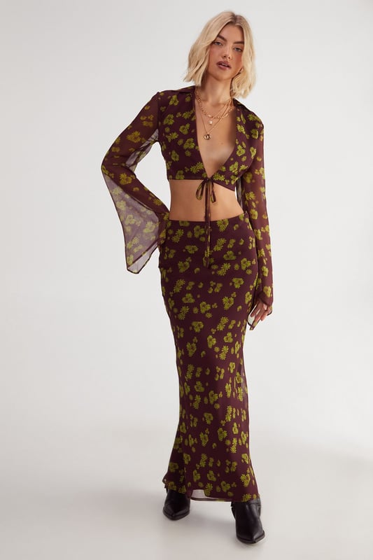 Chiffon fabric with a crinkle texture for added dimension
        Plunging V-neckline with tie-front detail
        Fluted sleeves for a dramatic flair
        Cropped length to showcase your midriff
        Ditsy floral print for a feminine touch
    
    Embrace the boho-chic aesthetic with this captivating Ditsy Crinkle Chiffon Tie Front Fluted Sleeve Crop Top from NastyGal. The lightweight chiffon fabric drapes beautifully, while the crinkle texture adds an intriguing visual element. The plunging V-neckline with a tie-front detail allows for adjustable coverage, making it perfect for various casual occasions. The fluted sleeves create a romantic silhouette, adding movement and grace to your ensemble. Pair this crop top with high-waisted jeans and ankle boots for a trendy daytime look, or style it with a flowing maxi skirt and sandals for a relaxed garden party. The versatile design makes it ideal for family gatherings, brunch dates, or casual outings with friends. Layer with delicate gold necklaces to complement the neckline and add a touch of glamour to this effortlessly stylish piece.