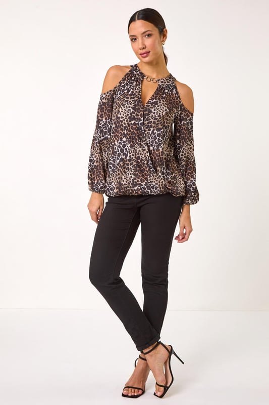 Animal Print Cold Shoulder Stretch Top from Roman. Show off a touch of skin with this stylish cold shoulder top in a trendy animal print. Featuring a chic wrap front design and long sleeves with elasticated cuffs for added detail. The flattering balloon hem adds a touch of sophistication, while the trim at the neck and the round neck with 2 button fastening at the back neck complete the look. Style effortlessly with tailored trousers and heeled boots for a fashionable ensemble perfect for the Autumn/Winter season.