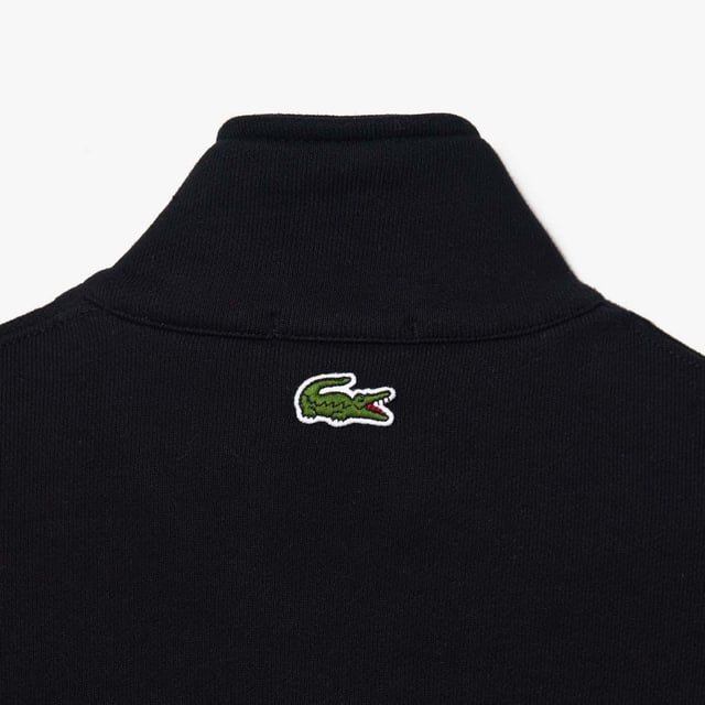 Unisex Lacoste Loose Fit High Neck Sweatshirt in Black. Finest materials, brand’s singular expertise. The perfect expression of Lacoste’s timeless wardrobe.- Loose fit is loose ease on body and sleeves, lower shoulders and armholes.- Half zipped sweatshirt in organic heavy French terry with big croc 80' on chest.- Unisexe.- Zipped high collar in shell fabric.- 7cm iconic original badge crocodile.- 3cm green crocodile at under middle back collar. Material: 100% Organic Cotton. Ref: SH0069031.