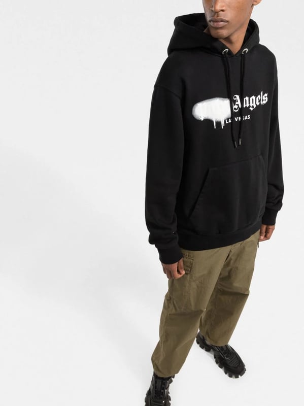 Palm Angels reemplaza su logotipo cl�sico con esta versi�n de Las Vegas, realzada con un efecto de pintura en aerosol en color blanco sobre un fondo negro s�lido. Confeccionada con algod�n suave, esta selecci�n SS22 tiene un corte relajado que encarna la est�tica de la marca y se completa con un pr�ctico bolsillo canguro en el centro.