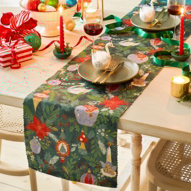 Get into the Christmas spirit with this wonderfully festive table runner. Featuring a digital printed design on woven polyester fabric of Christmas foliage and traditional tree decorations, including vintage baubles, candles and even a swan in vivid seasonal colours. This beautiful table runner will transform and add some instant seasonal cheer to your Christmas dining table.