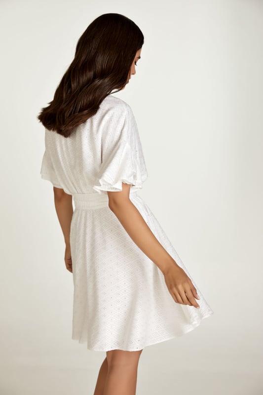 Este vestido blanco está confeccionado en tejido de viscosa bordado tono sobre tono. Tiene mangas cortas con doble volante y hombros caídos. Tiene escote redondo con abertura en V en la parte delantera. Debajo del busto hay una costura curva bajo la cual el vestido se abre en forma de campana. Hay una cremallera oculta en el interior que permite ponerse el vestido fácilmente. Está forrado. El vestido se puede llevar con o sin cinturón que está confeccionado en el mismo tejido. El cinturón está incluido.