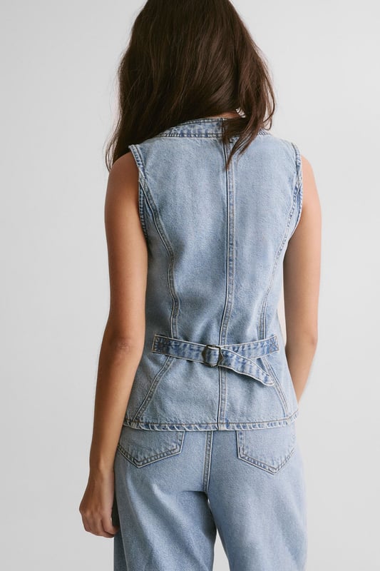 Sleek longline silhouette for a contemporary twist on classic denim
        Plunging V-neckline adds a touch of allure
        Button-front closure for easy wear and versatile styling
        Fitted waist with adjustable belt detail for a customised fit
        Crafted from sturdy denim fabric for long-lasting wear
    
    The Longline Denim Waistcoat from NastyGal is a versatile piece that seamlessly blends casual cool with a hint of sophistication. This sleeveless wonder can be styled in myriad ways to suit various occasions. For a laid-back daytime look, pair it with wide-leg jeans and trainers, as seen on our model. Layer it over a crisp white shirt and tailored trousers for a smart-casual ensemble perfect for family gatherings or informal work events. The adjustable belt allows you to cinch in the waist for a more defined silhouette, while the longline cut provides flattering coverage. Whether worn open as a vest or buttoned up as a standalone top, this denim waistcoat is sure to become a staple in your wardrobe, offering endless styling possibilities for the fashion-forward individual.