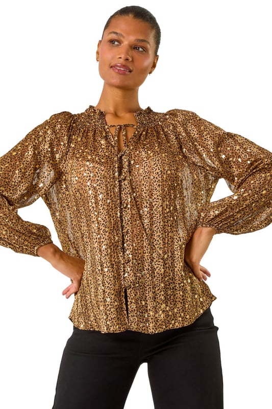Tie Front Animal Print Blouse from Roman. Embrace your wild side this Autumn/Winter in this stunning animal print blouse. The all over print is elevated with metallic gold spots for a touch of glamour, while the V-Neck and button through front create a chic look. Long sleeves keep you warm, and the tie front detail adds a fun twist to this versatile piece. Pair with pleather trousers and heeled boots for a party ready ensemble that's sure to turn heads!