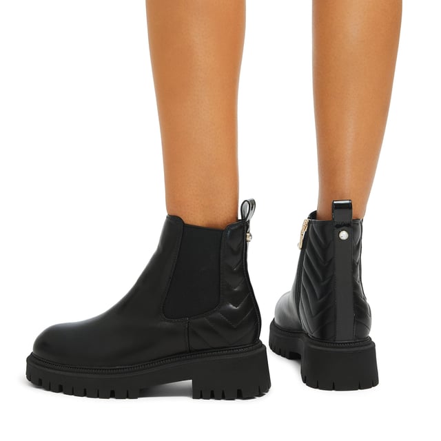 This Carvela Ace Chelsea ankle boot features a black upper with chevron overstitch quilting at the back of the ankle. There is a crystal stud at the back of the ankle with a small patent pull tab.