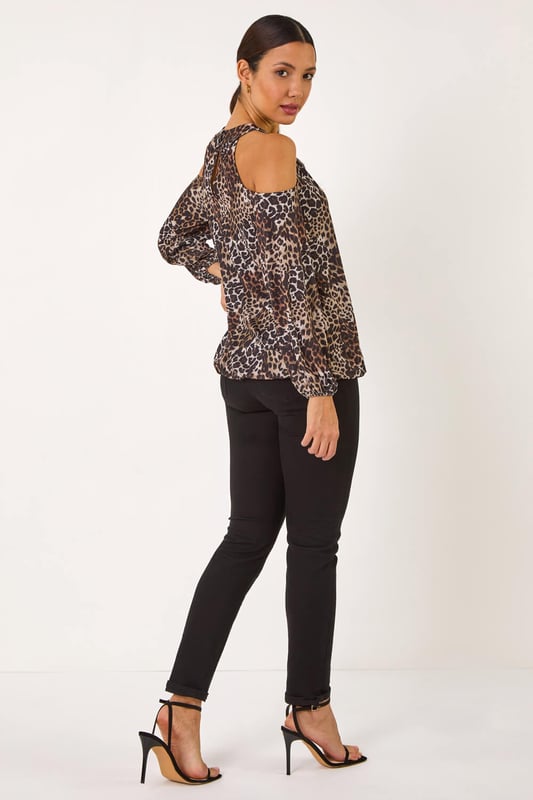 Animal Print Cold Shoulder Stretch Top from Roman. Show off a touch of skin with this stylish cold shoulder top in a trendy animal print. Featuring a chic wrap front design and long sleeves with elasticated cuffs for added detail. The flattering balloon hem adds a touch of sophistication, while the trim at the neck and the round neck with 2 button fastening at the back neck complete the look. Style effortlessly with tailored trousers and heeled boots for a fashionable ensemble perfect for the Autumn/Winter season.