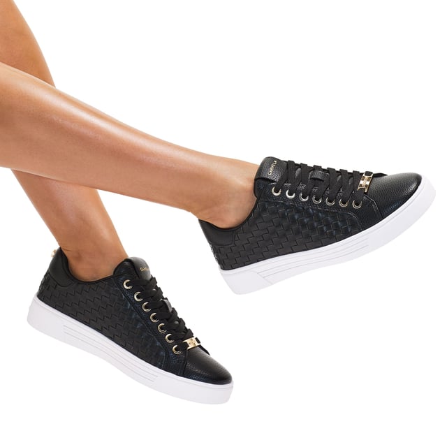 The Carvela Daze Weave trainer features a black upper with woven sides. The hardware is gold with embossed foil logo on the tongue.