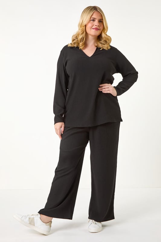 Curve Stretch V-Neck Collared Top from Roman. Elevate your casual style with this V-Neck jersey top, perfect for the Autumn/Winter season. Crafted from a textured jersey fabric, this top features a classic V-Neckline with a collar detail and comfortable long sleeves. The below hip length offers a flattering silhouette that pairs effortlessly with the matching trousers for a coordinated look. Complete your outfit with boots and a jacket for a chic and cozy ensemble.
