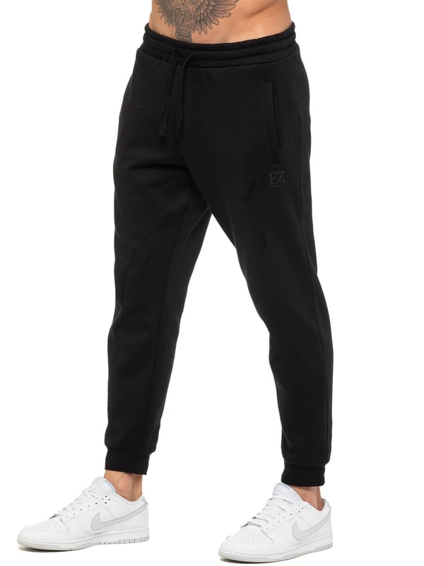 Enzo Mens Regular Fit Joggers. Elasticated Waistband With Adjustable Drawstring. Features 2 Side Slash Pockets & Single Welt Back Pocket. Cuffed Ankle. Features EZ Logo.