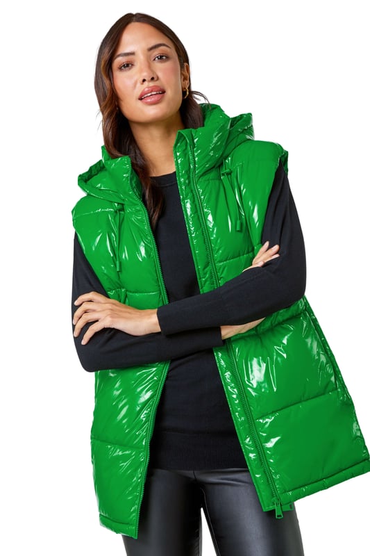 Patent Hooded Gilet from Roman. Add a pop of colour and a unique twist to your casualwear with our bold hi-shine gilet! The perfect layer for transitioning into Autumn, this cosy staple has a padded silhouette and cosy funnel neckline for warmth. With a secure zip fastening, this jacket also has drawstring detail and a glossy high shine finish. This statement jacket is a fashionable yet functional layering piece with zipped side pockets and a showerproof hood. Wear over relaxed denim and lightweight jumper for your own runway inspired outfit!