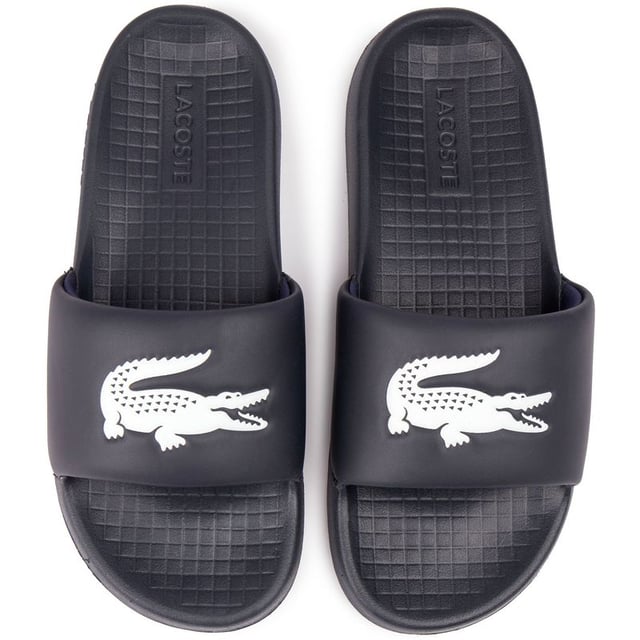 Lacoste Serve Slide Sandalias Saluda a este elegante y cómodo par de chanclas de estilo de vida, las Serve Slides de Lacoste. Perfectas para tus días en la piscina, visitas al spa o simplemente como un básico diario de verano, estas sandalias te tienen cubierto. Ponte las elegantes sandalias azules y siente la comodidad de una correa superior acolchada suave y flexible y una plantilla moldeada y acolchada que abraza tus pies. El diseño elegante y minimalista presenta la famosa marca llamativa en la correa ancha. Muestra tu estilo relajado y tus looks de clima cálido.