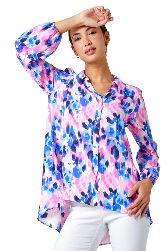 Abstract Print Dropped Hem Blouse from Roman. This sophisticated dropped hem blouse is cut from a smooth woven fabric and adorned in a colourful abstract print. It features a fully open front complete with button fastenings, full length cuffed sleeves and a smart collared neckline. A flattering dropped hem provides extra coverage at the back. Pair with cropped stretch trousers and heels for an evening out or add smart trousers and courts for work wear chic!