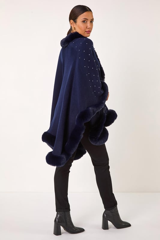 Hotfix Faux Fur Trim Cape from Roman. This style is ONE size.  Wrap up in style this Autumn and Winter with this all over hotfix faux fur trim cape. In a classic black hue with dazzling silver hotfix detailing, this cosy cape is the perfect layering piece. Simply throw on over a t-shirt and jeans for an effortlessly chic and stylish look.