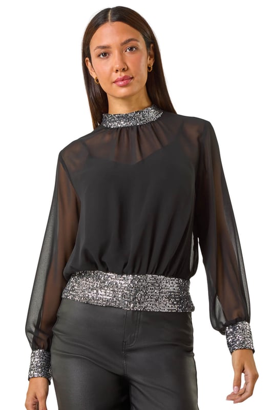 Sequin Detail Top from Roman. Shine bright in this glamourous sequin detail top, perfect for the Autumn/Winter season. Crafted from a delicate chiffon fabric, this top features intricate sequin detailing on the neck, cuffs, and hem for a touch of sparkle. The high neck and long sleeves add an elegant touch, while the included jersey cami provides coverage. Pair with tights and a skirt for a chic and festive look that will turn heads wherever you go!