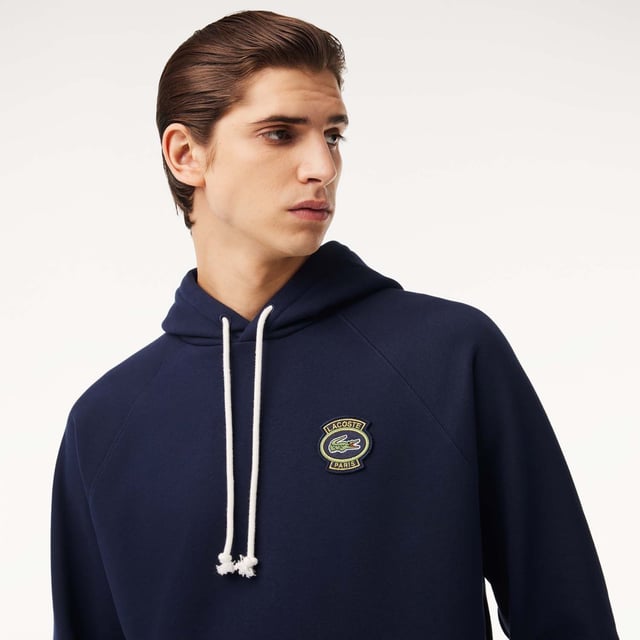Own the french fashion sport Hoodie in French Terry Raglan sleeves Kagaroo pocket Knot drawcord 55x53 cm felt badge with Lacoste Paris embroidery and green crocodile on chest.