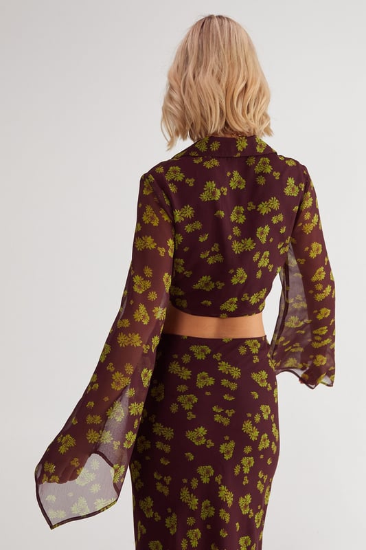 Chiffon fabric with a crinkle texture for added dimension
        Plunging V-neckline with tie-front detail
        Fluted sleeves for a dramatic flair
        Cropped length to showcase your midriff
        Ditsy floral print for a feminine touch
    
    Embrace the boho-chic aesthetic with this captivating Ditsy Crinkle Chiffon Tie Front Fluted Sleeve Crop Top from NastyGal. The lightweight chiffon fabric drapes beautifully, while the crinkle texture adds an intriguing visual element. The plunging V-neckline with a tie-front detail allows for adjustable coverage, making it perfect for various casual occasions. The fluted sleeves create a romantic silhouette, adding movement and grace to your ensemble. Pair this crop top with high-waisted jeans and ankle boots for a trendy daytime look, or style it with a flowing maxi skirt and sandals for a relaxed garden party. The versatile design makes it ideal for family gatherings, brunch dates, or casual outings with friends. Layer with delicate gold necklaces to complement the neckline and add a touch of glamour to this effortlessly stylish piece.