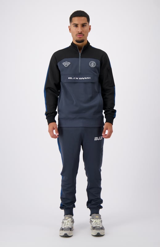 100 % poliéster Cuello alto con media cremallera Camino de convoy en el pecho Bolsillo lateral con cremallera en el brazo izquierdo Solapa distintiva de BNNS en color negro Dos bolsillos delanteros con cremallera Mangas a rayas Se puede combinar con RUMBLE TRACKPANTS