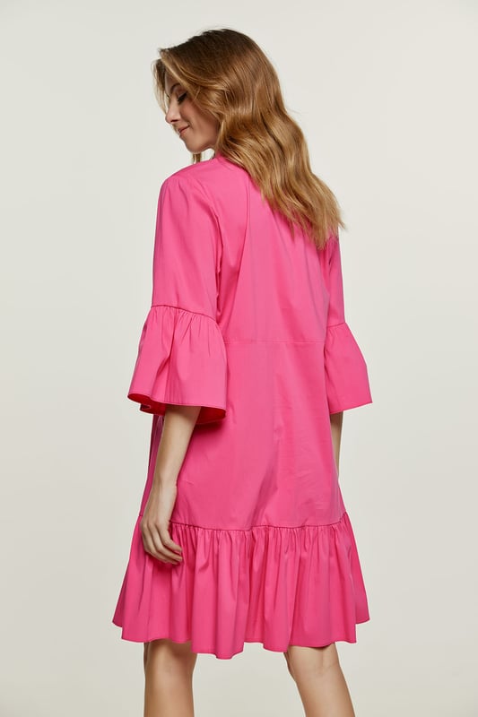 Deze fuchsia jurk is gemaakt van geweven stretch poplin. Het heeft klokkende mouwen van ¾ lengte. De jurk heeft een kraag en een sluiting in de taille met plastic knopen. Een naad onder de buste zorgt voor een perfecte pasvorm. De jurk heeft een brede zoom met ruches. De jurk heeft een losse pasvorm en valt boven de knie.