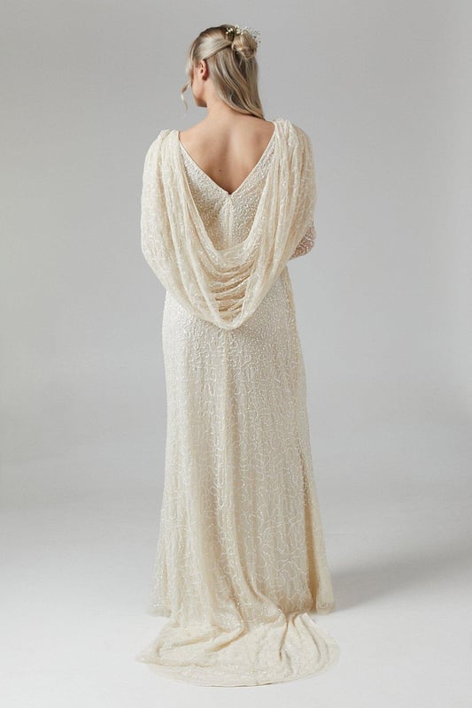 Exquisite hand-stitched embellishments for a luxurious finish
        Elegant V-neckline complemented by long sleeves
        Stunning cowl back detail for added sophistication
        Floor-length design with a graceful silhouette
        Maternity-friendly cut to accommodate and flatter your changing shape
    
    Radiate bridal elegance in this captivating maternity wedding dress from Coast. The hand-stitched embellishments create a dazzling effect, perfect for catching the light as you walk down the aisle. The V-neckline and long sleeves offer a timeless appeal, while the cowl back adds a touch of drama to your ensemble. Designed with the expectant bride in mind, this gown gracefully accommodates your changing silhouette, ensuring comfort throughout your special day. Style with delicate drop earrings and a simple bracelet to let the dress take centre stage. For a complete bridal look, consider a floor-length veil and ivory satin heels. This gown is not just for the ceremony; it transitions beautifully to the reception, allowing you to dance the night away in style and comfort.