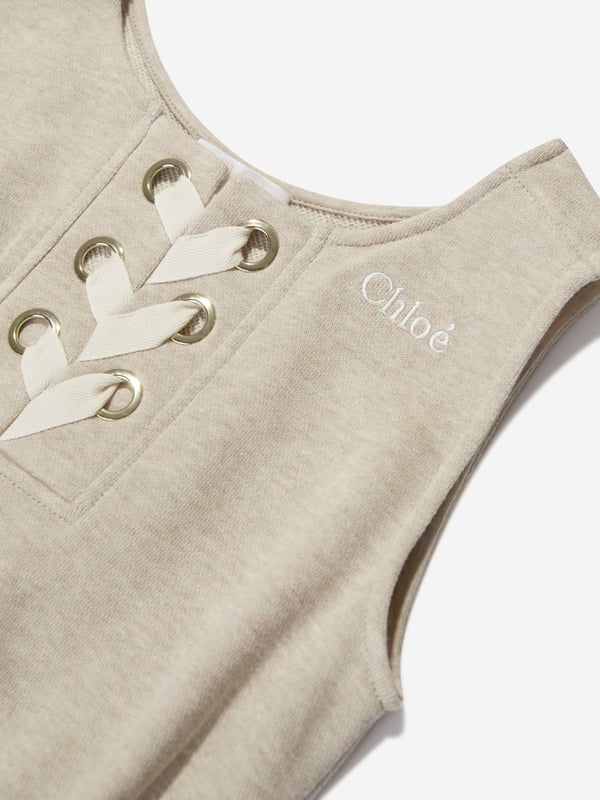 Chloé Girls Sleeveless Playsuit in Beige Chloé portray demure whimsical subjects in their exquisite aesthetics. This girls sleeveless jumpsuit is depicted in unbrushed fleece cotton via lacing at the front, golden trims, large embroidery Chloé on the chest, elasticated waist and piped pockets. She will look and feel divine. 100% Organic Cotton Sustainable