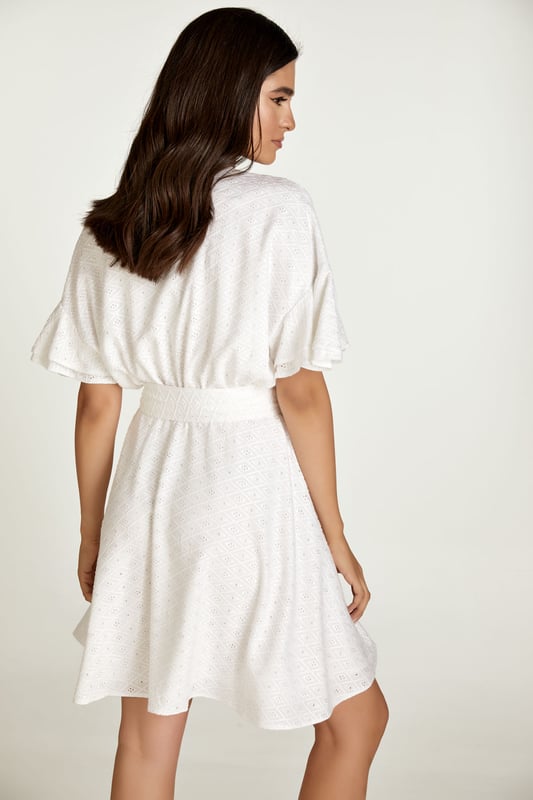 Este vestido blanco está confeccionado en tejido de viscosa bordado tono sobre tono. Tiene mangas cortas con doble volante y hombros caídos. Tiene escote redondo con abertura en V en la parte delantera. Debajo del busto hay una costura curva bajo la cual el vestido se abre en forma de campana. Hay una cremallera oculta en el interior que permite ponerse el vestido fácilmente. Está forrado. El vestido se puede llevar con o sin cinturón que está confeccionado en el mismo tejido. El cinturón está incluido.