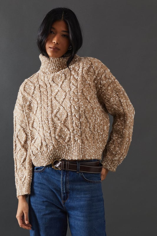 Intricate cable knit pattern for a textured look
        Cosy roll neck design for extra warmth
        Relaxed, oversized fit for comfort and style
        Dropped shoulders for a contemporary silhouette
        Ribbed cuffs and hem for a snug finish
    
    This Cable Knit Roll Neck Jumper from Warehouse is the epitome of casual chic. The intricate cable knit pattern adds depth and interest to your outfit, while the oversized fit creates a relaxed, effortless vibe. Perfect for those chilly autumn days or cosy winter evenings, this jumper is versatile enough to dress up or down. For a laid-back look, pair it with wide-leg jeans and trainers, as shown in the image. To dress it up a bit, try tucking the front into a leather midi skirt and adding ankle boots. The neutral tone makes it easy to style with various colours and textures in your wardrobe. Whether you're heading to a casual family gathering or meeting friends for a coffee, this jumper will keep you warm and stylish. Its timeless design ensures it will remain a staple in your wardrobe for seasons to come.