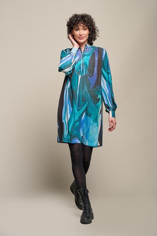 Stijlvolle damesjurk met verfijnde details en unieke printDe Dhalia Print Jurk is een schitterend en elegant kledingstuk met oog voor detail. De semi-transparante stof geeft een luchtig en verfijnd effect, terwijl de voering zorgt voor comfort en ondoorzichtigheid tijdens het dragen. De olieachtige print straalt in diverse kleuren, waaronder paars, aquagroen en een zwarte achtergrond, wat een eigentijdse en trendy uitstraling toevoegt. De prachtig uitgewerkte details, zoals het opstaande kraagje met plastron en bedekte knoopjes, de pofmouwen met manchetten en dezelfde verfijnde knoopjes, evenals de luxe plooien en piping bij de schoudernaden en rugpas, dragen bij aan de geraffineerdheid van het ontwerp. De jurk heeft een wijd uitlopende, lange blouse-stijl die zorgt voor een flatterend en elegant silhouet. De subtiele steekzakken in de zijnaden voegen een comfortabel element toe aan deze chique printjurk, waardoor de jurk zowel elegantie als functionaliteit combineert. Met zijn opvallende print, pofmouwen en prachtige details is deze jurk een veelzijdige aanvulling op elke garderobe. Op zoek naar extra warmte in de winter? Combineer de jurk met het aquagroene Parker vest voor een opvallende en stijlvolle look. Deze printjurk is absoluut een waardevolle toevoeging aan je nieuwe garderobe!"