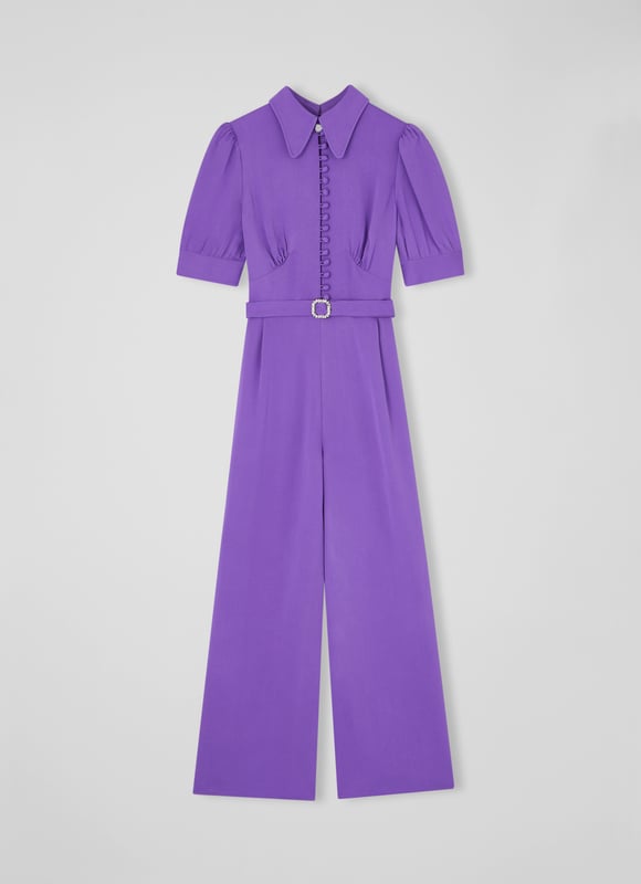LK Bennett Aldous Dresses, Wisteria The Aldous jumpsuit in the Royal Ascot x LKB collection is crafted from a silky fabric in wisteria purple. It has a long rounded collar, puff shoulder short sleeves, a half placket of covered buttons, a diamante buckle belt, and wide leg cropped trousers.