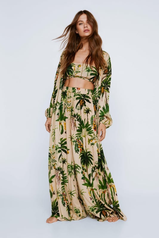 Vacation pending. Feel fierce in our three piece set, which features a bandeau top, extreme wide leg pants, and a maxi length kimono, in a fun palm tree print. Pairs well with sandals and sunglasses for a summer look that will turn heads. Crinkle Palm Tree Bandeau And Maxi Kimono 3pc Pants Set High Quality Crinkle Fabric Flattering Wide Leg Pants Flirty Cropped Bandeau Top Statement Floor Length Kimono Head Turning Palm Tree Print Model wears a size M (US size 6/UK size 10).