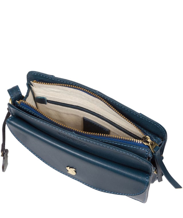 The 'Magda' cross body bag from Conkca London is handcrafted from multi-toned leather for a beautiful finish. A zip-over top opens to reveal a spacious compartment with two slip pockets, lined with natural and untreated 100% cotton. Features a pocket on the front secured with a magnetic press-stud and a slip pocket on the rear, ideal for a smartphone. Comes with an adjustable leather strap with a maximum drop length of 68cm. Adorned with the inimitable Conkca squirrel charm and Conkca logos.