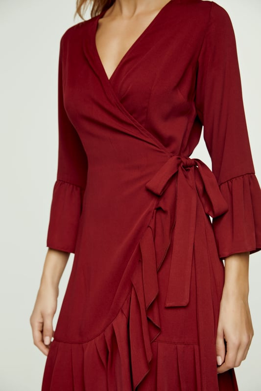 Deze wijndress is vervaardigd uit geweven viscose. Het heeft een V-hals en 3/4 klokmouwen. Deze wikkeljurk heeft een strik aan de linkerkant die door een gat aan de rechterkant wordt geregen en vastgebonden wordt met de strik aan de rechterkant opzij of op de rug. Er is een ruche langs de zoom van ongeveer 15 cm. De maten voor maat 36/S (in cm) zijn: Schouderbreedte-33, Buste-42, Taille-42, Zoom-70, Mouwlengte -Lichaamslengte-95/100. 100% viscose