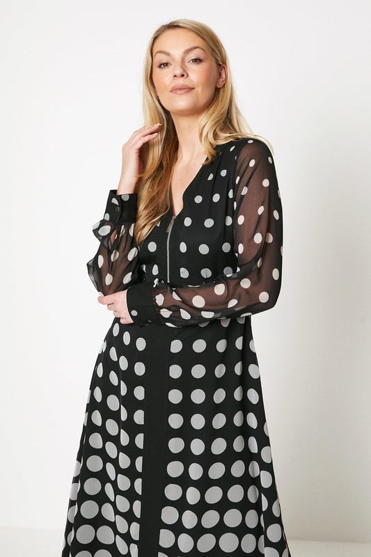 Zip front midi dress crafted from woven fabric
Flattering V-neckline with long sleeves
Allover polka dot print in a contrasting border pattern
Flared A-line skirt with a swishy midi length
Effortless pull-on style for easy dressing

This polka dot midi dress exudes sophistication with its striking border print and feminine silhouette. The zip front design offers a modern twist, while the flared skirt creates a flattering shape. Style with heeled sandals and a clutch for a chic daytime look perfect for casual events or family gatherings. The woven fabric ensures a comfortable yet glamorous feel.