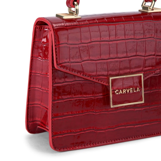 This Carvela Jessica Top Handle Bag features a deep red exterior with large croc print. There is a gold branded plate on the front flap. Dimensions: 15cm (H), 17cm (L), 7cm (D). Strap length: 125cm.