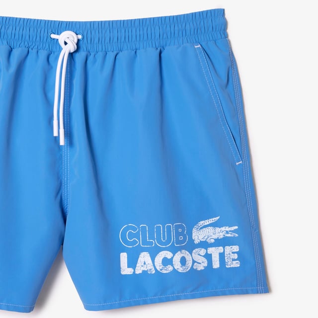 The essential swimwear of Lacoste wardrobe Short length short  mid-thigh when worn. Solid recycled polyester Quick dry Full elasticated waistband adjustable with drawcord and an integrated mesh boxer to ensure freedom and ease of movement in all circumstances. 2 hips side pockets 1 back piped pocket at right side when worn 1 inside hidden pocket at waistband with velcro Embroidered eyelets at waistband Branded drawstring 3 cm recycled tone on tone crocodile at back pocket Underpant thigh binding with Lacoste wording Contrasted white topstitches on garment Lacoste club vintage effect print on fornt left leg when worn Goes with a branded swimbag made of solid ripstop recycled fabric