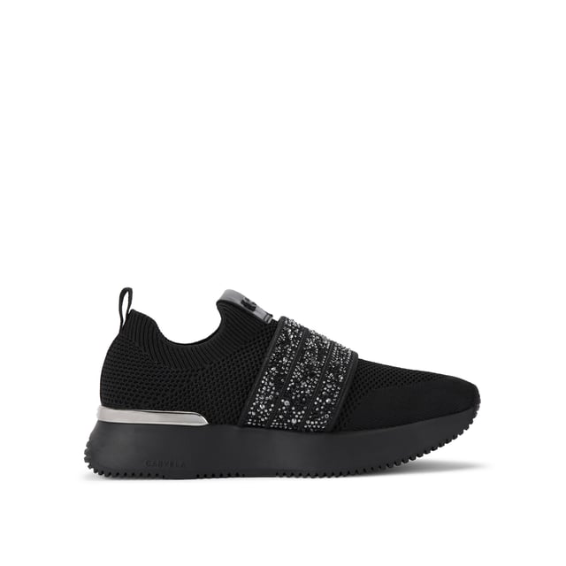 The Carvela Flare Sparkle trainer is a slip-on style with a black knitted upper. There is a crystal encrusted black fabric strap across the foot. The sole is chunky in black.