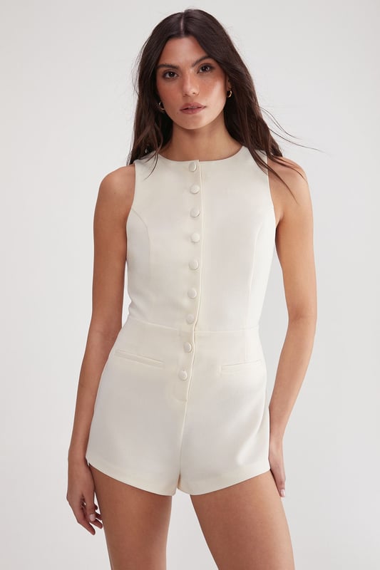Sleek tailored playsuit for a polished look
        High neckline and sleeveless design for a professional appearance
        Fitted waist to accentuate your silhouette
        Striking open back with elegant tie detail
        Short length perfect for warmer office environments
    
    Make a statement in the boardroom with this chic Essentials Tailored Playsuit from NastyGal. This versatile piece seamlessly blends sophistication with contemporary style, making it an ideal choice for the modern professional. The high neckline and sleeveless cut offer a refined look, while the tailored fit flatters your figure. The playsuit's short length adds a touch of modernity, perfect for navigating warm office spaces with ease. For a polished workwear ensemble, pair it with a structured blazer and classic court shoes. Alternatively, dress it down for after-work drinks by swapping the blazer for a lightweight cardigan and adding some statement jewellery. The unexpected open back with its elegant tie detail adds a subtle hint of allure, ensuring you transition effortlessly from day to evening events.