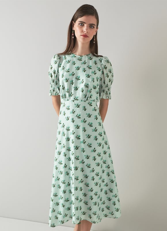 The Tabitha dress is crafted from a silk-blend spot jacquard in morning mist green with a 1930's hand painted primula print reimagined from vintage archives. It has a round neck, puff shoulders, short shirred sleeves, pleating at the bust, a floaty shape and a dipped midi-length hem.