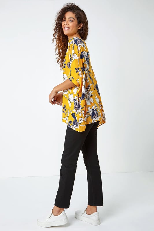 Floral Print Button Back Top from Roman. Add a light layer to your spring summer wardrobe with this short sleeve relaxed fit tee. Cut from a soft on the skin fabric, this boxy fit top is perfect for throwing on over your casual looks this season. Our large floral print top is finished with fabric covered buttons all down the back for added interest. Opt for white cropped trousers and sandals for your holiday ready ensembles.