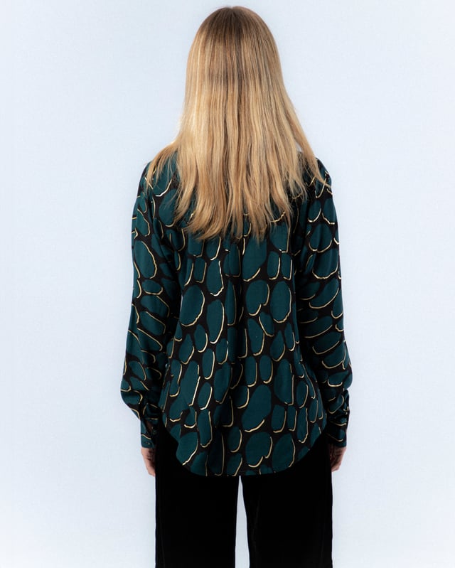 La camisa estampada Victoria te enamorará con su elegante color azul petróleo. Déjate envolver por el diseño sofisticado de la camisa Victoria.
 
 
 
 Blusa holgada con cuello solapa.
 
 Manga larga.
 
 Cierre frontal con botones.
 
 Detalle de tapete con botones en espalda.
 
 Tejido viscosa.
 
 Estampado Abstracto con detalles de foil dorado.