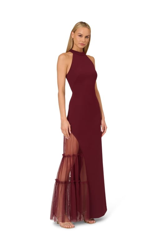 Raise a glass to celebrate all of your upcoming occasions in this eye-catching halter gown. This formal dress features a halter bodice, short mock neckline, and a fitted silhouette that is contrasted by a sheer mesh skirt with ruffle details. Designed with knit crepe that has some stretch and no waist seam for a comfortable and figure-flattering fit, this evening gown is perfect for a formal or black-tie dress code. A hidden zipper closure at the centre back completes this stunning dress. Styled with nude heels and a beaded clutch, this sexy yet sweet gown is a head-turner.