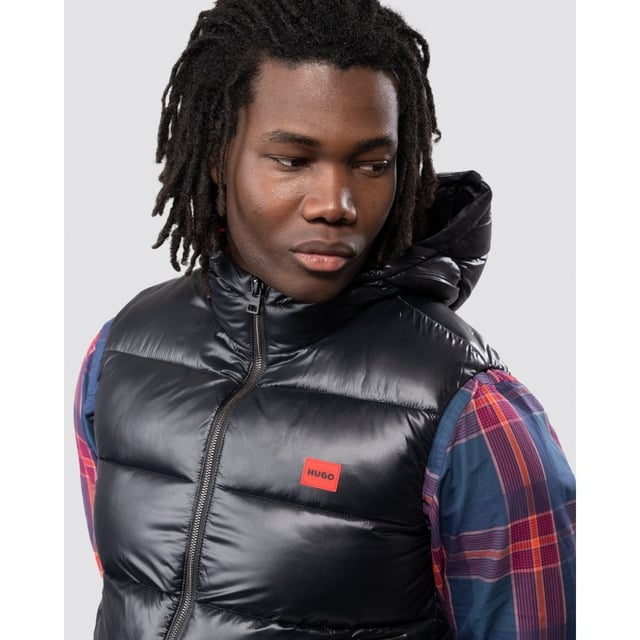 This sporty Water Repellent Puffer Hooded Gilet from HUGO is the perfect piece to elevate your wardrobe this season with sustainable style. Crafted from water-repellent recycled nylon and padded with sustainably sourced recycled fibres providing warmth and comfort. Featuring an insulated hood with full zip closure, elasticated binding and front zip pockets. Finished with a signature HUGO logo patch on the chest.Slim Fit, Water-Repellent Recycled Nylon Shell, Recycled Polyester Padding, Insulated Hood, Full Zip Closure, Twin Zip Front Pockets, Internal Zip Pocket, HUGO Branding. -Style & Fit:Slim Fit, Fits True to Size. Composition & Care:Shell: 100% Recycled Polyamide, Fill: 100% Recycled Polyester, Machine Wash.
