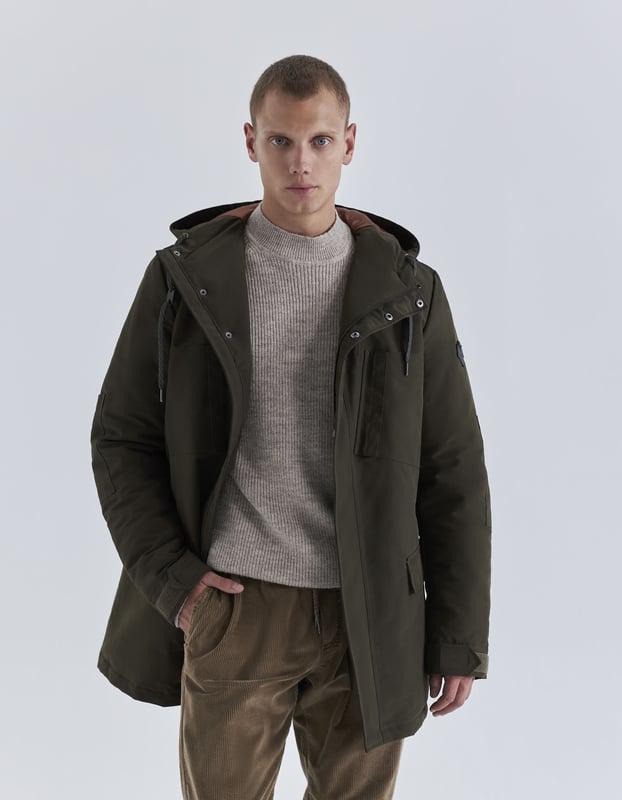 This khaki parka has high collar, hood, long sleeves and multi-pockets with drawstrings to tie at hood, concealed zip and press stud fastening under placket.