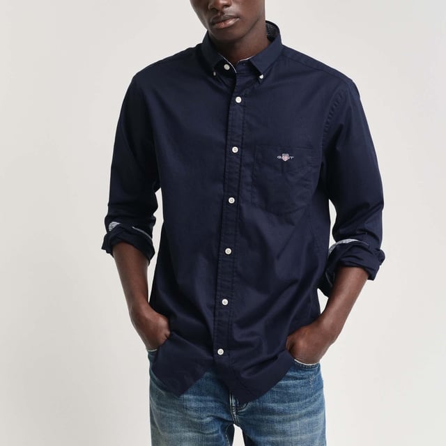 The shirt is made from durable poplin fabric  and is a true classic for your preppy wardrobe. Featuring a rounded hem and an embroidered 1980s-style GANT crest graphic on the chest pocket.